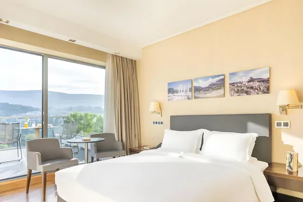 Manželská postel a balkon v ukázkovém pokoji The Athens Gate Hotel