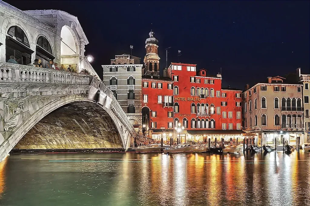Rote Fassade des Hotels Rialto und Rialtobrücke bei Nacht